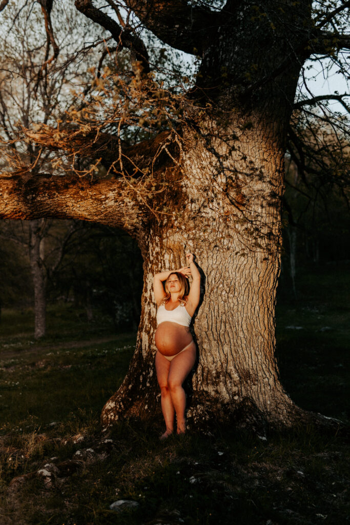 Lisa Ajax gravid som lutar sig mot ett träd