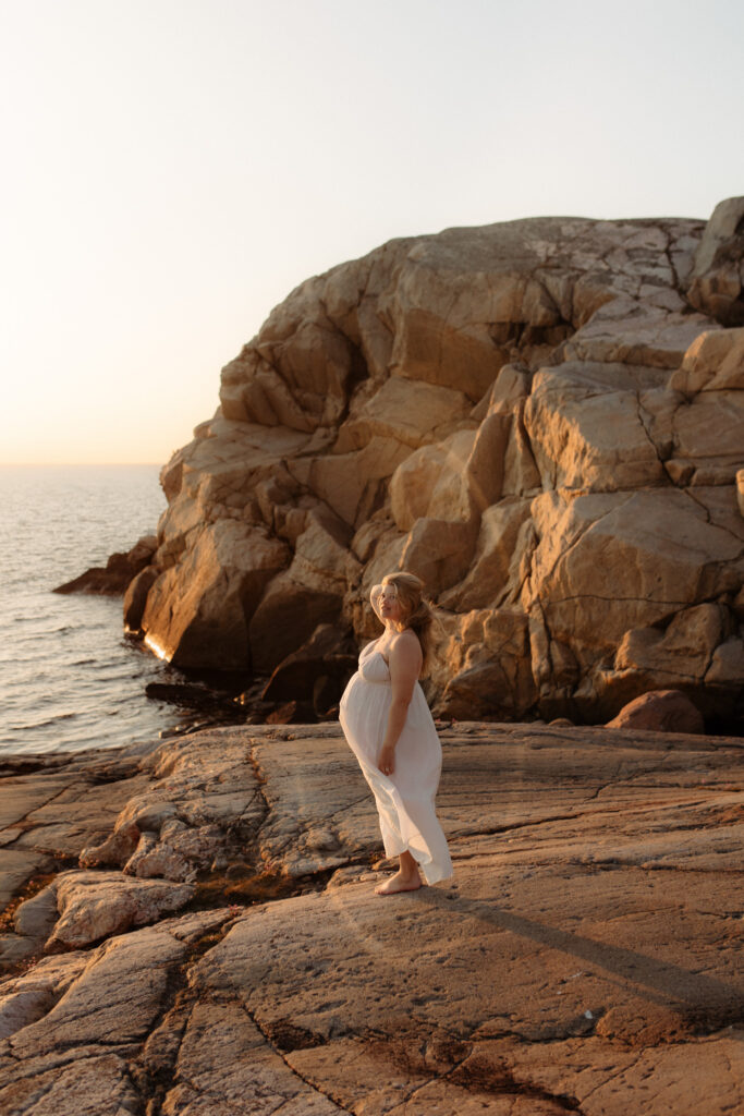 en mamma står på klippor i västkusten och kolla mot havet i solnedgången