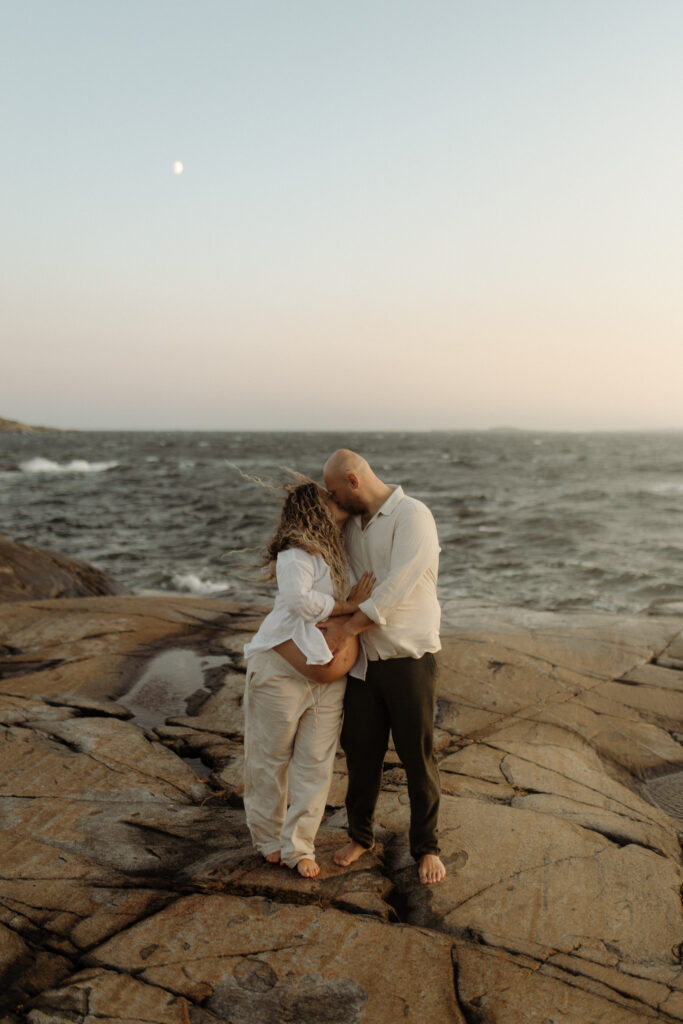 en gravid kvinna och hennes partner håller om varandra i månskenet med havet bakom dom