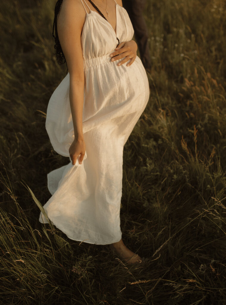 en kvinna i en vit klänning som böljar i vinden håller om sin gravidmage
