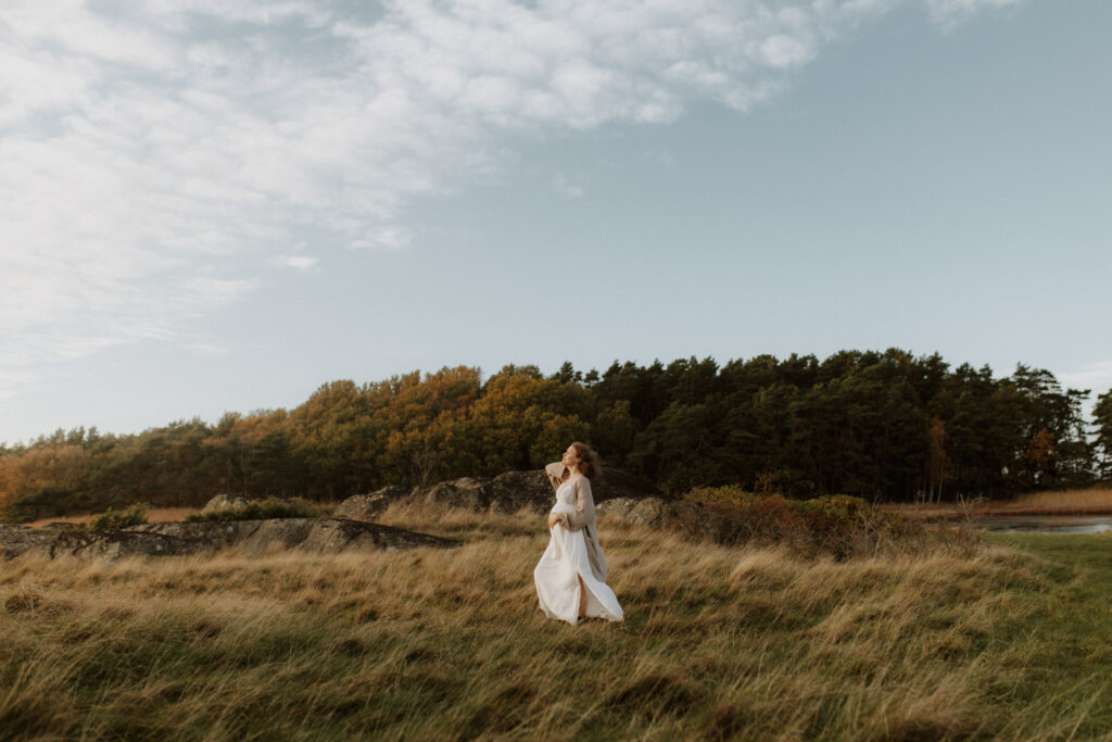en gravid mamma står på ett öppet fält med vind i håret och håller om sin mage