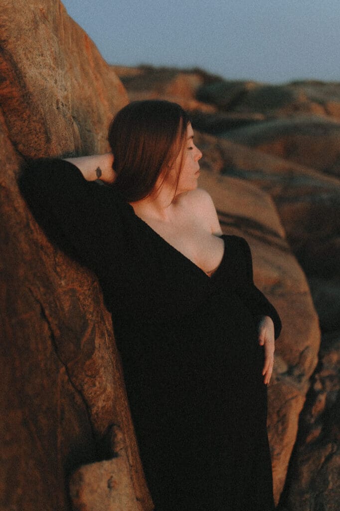gravid kvinna i svart gravidklänning lutar sig mot den röda klippan