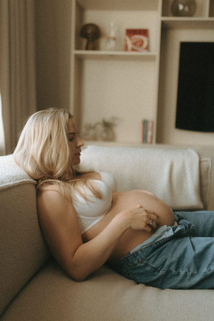 gravid kvinna vilar i soffan hemma i mjukt fönsterljus