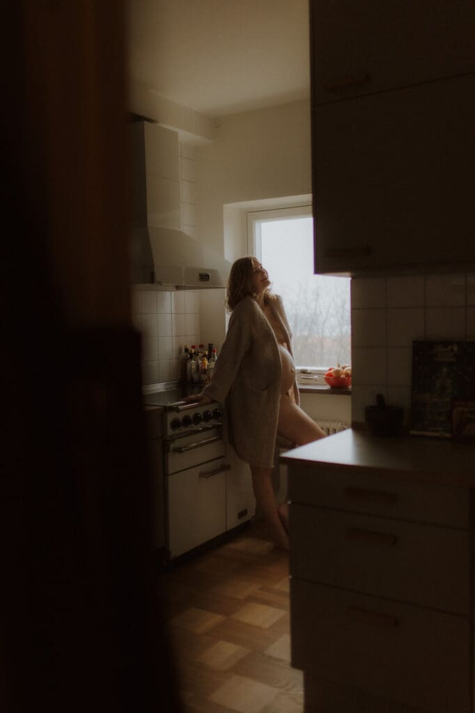 en gravid kvinna lutar sig mot köksbänken med snö som faller utanför fönstret