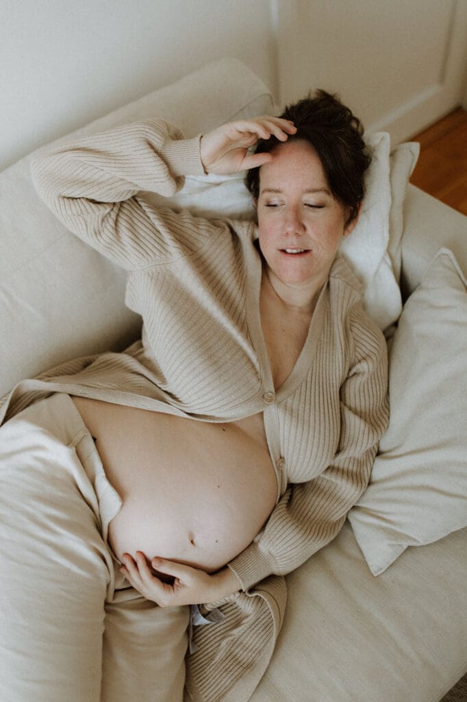 gravid mamma i sängen bland vita lakan och en stickad kofta