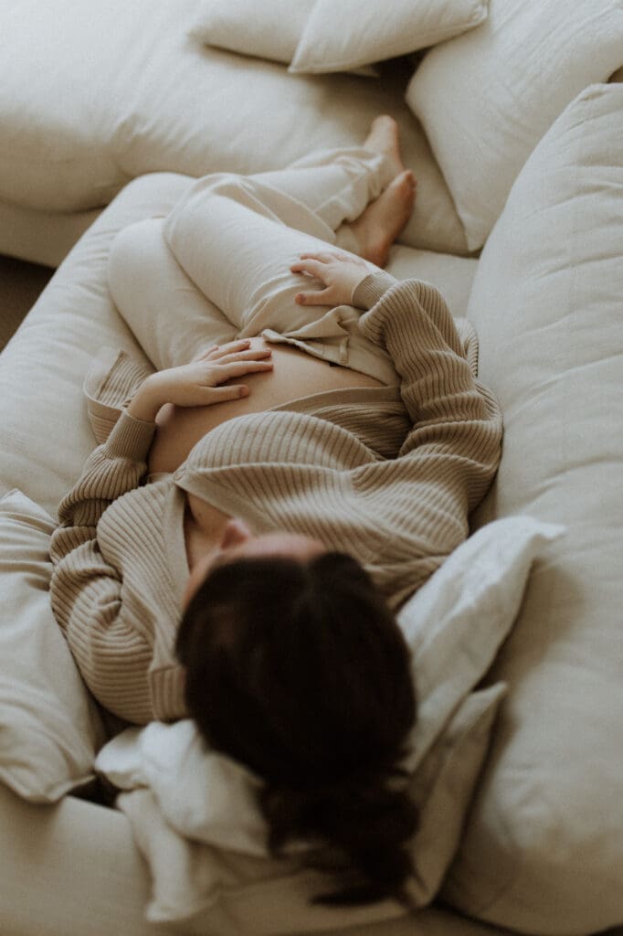 gravid kvinna i beige stickat ligger i sängen, fotograferad ovanifrån