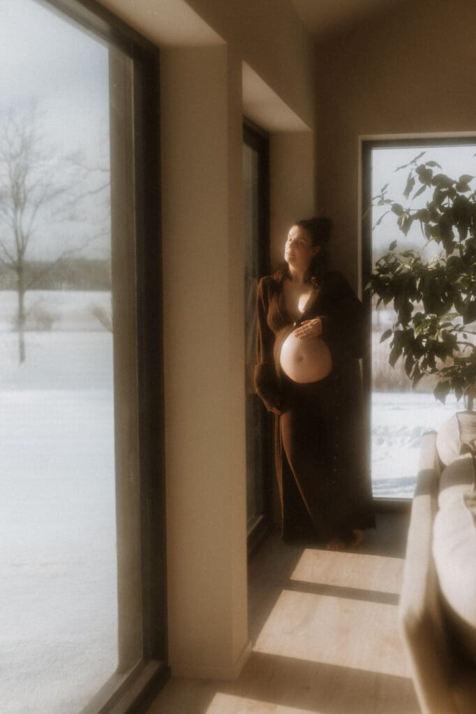 en mamma står och håller om sin gravida mage och tittar ut mot snön