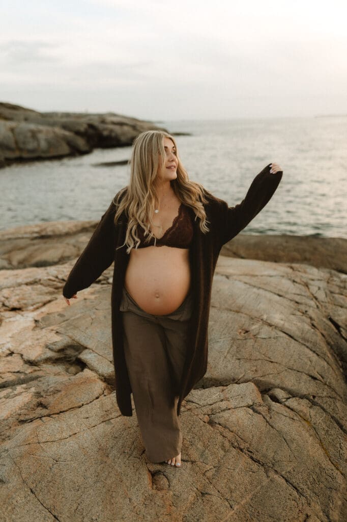 gravid kvinna går på klipporna vid havet i lång mörk kofta en blåsig vinterdag