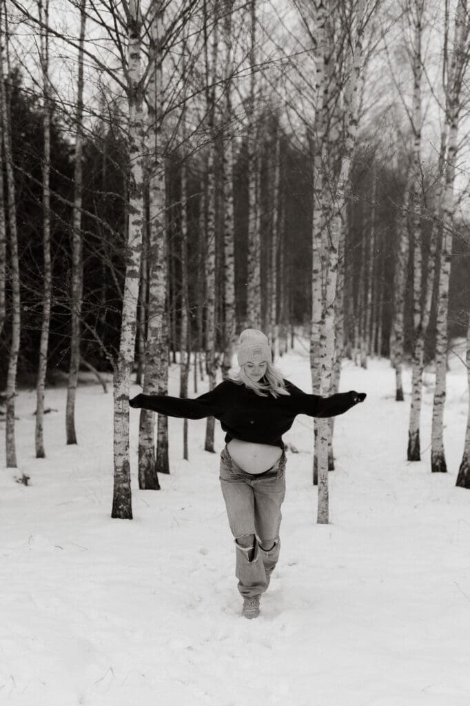 en gravid kvinna i jeans och hoodie springer över ett snöfält